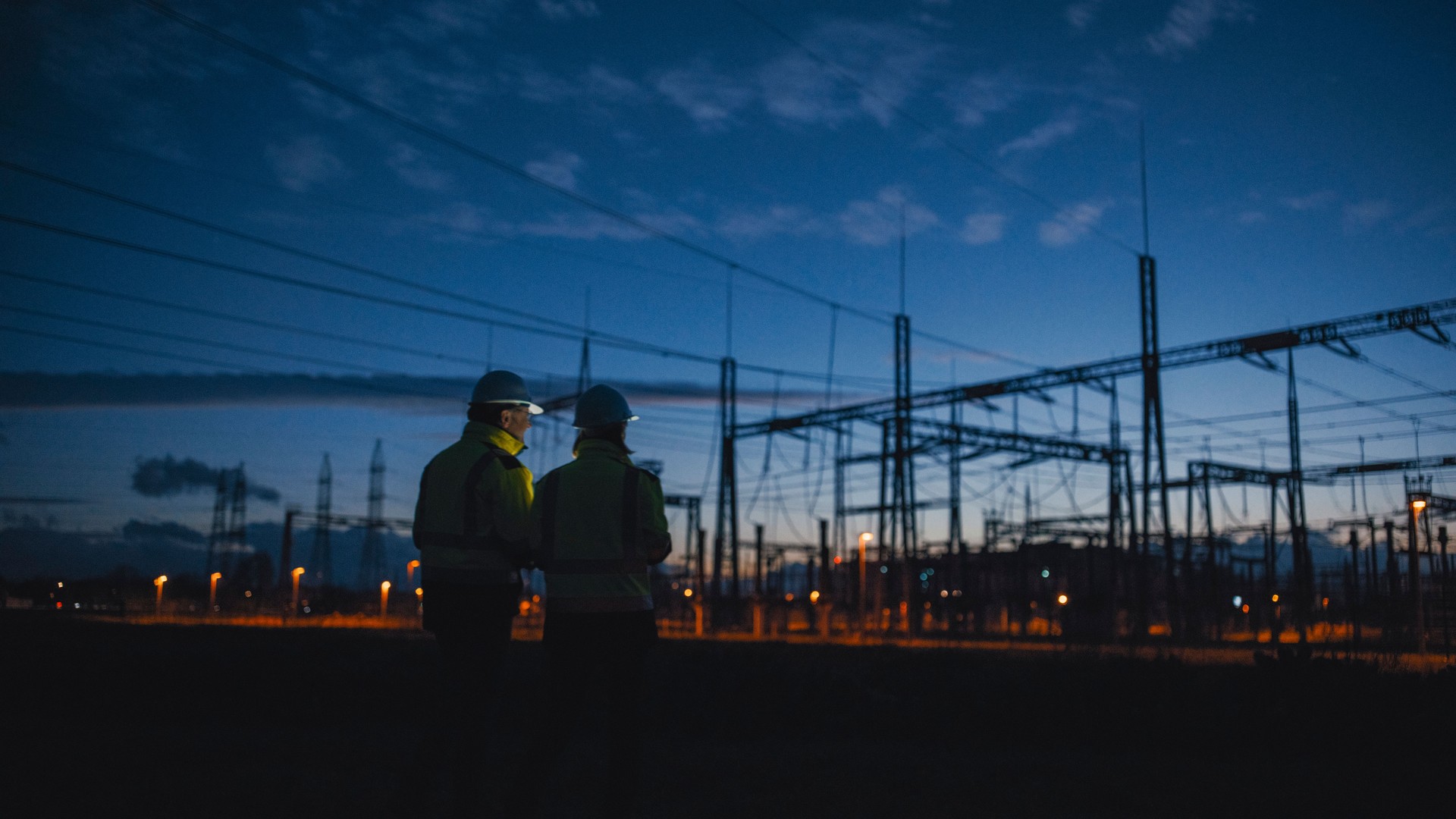 Rear View Of Determined Electrical Engineers Looking At Silhouette Transformers At Night